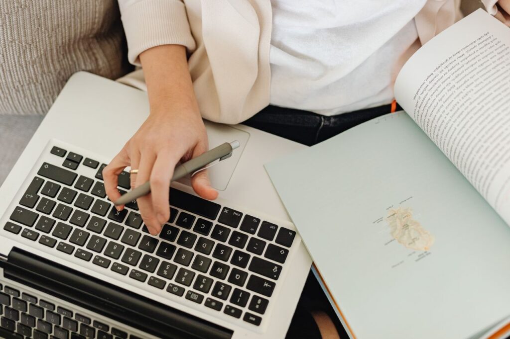 pexels photo 6632623 Close-up of a person working on a laptop and reading an open book. Ideal for educational themes.