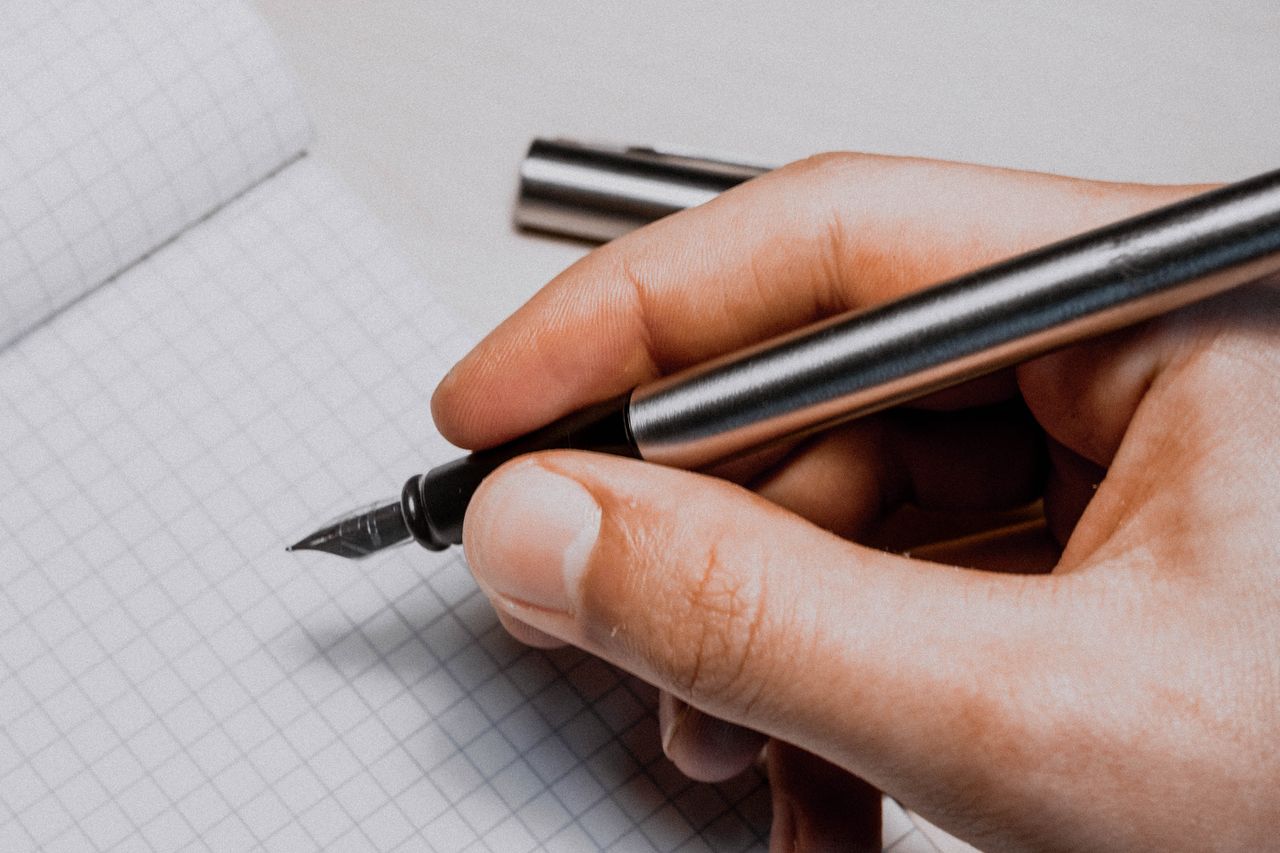 Home A detailed shot of a hand holding a fountain pen over graphing paper, suggesting creativity and planning.