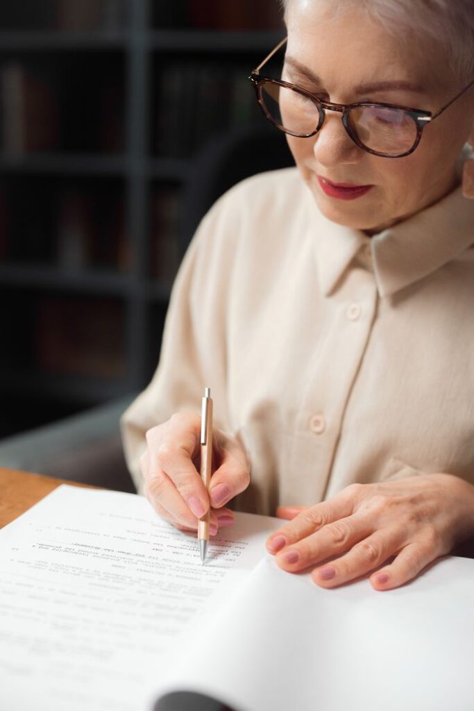 pexels photo 7967593 Elderly woman reviewing a script while writing at a desk indoors, showcasing professional expertise.